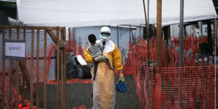 Figura 2. Un trabajador sanitario, con traje de protección para evitar el contagio de Ébola, atiende a un niño enfermo en la epidemia de Sierra Leona. (Crédito: John Moore). https://www.infosalus.com/salud-investigacion/noticia-analisis-brote-ebola-20150619074435.html